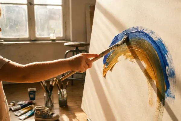 Kinderhand mit Pinsel malt kräftigen Farbschwung auf Leinwand in sonnendurchflutetem Berliner Kunstatelier.